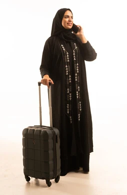 التواصل مع العائلة والأصدقاء, بورتريه لإمرأة عربية خليجية سعودية ترتدي العباءة السوداء تمسك حقبة السفروالهاتف المحمول تقوم بإجراء مكالمة هاتفية، صورة الجسم بالطول الكامل, خلفية بيضاء