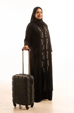 الشعور بالسعادة والفرح، السياحة في إجازة الصيف, بورتريه لشابة عربية خليجية سعودية محجبة ترتدي العباءة السوداء تمسك حقيبة السفر بإيماءات الحماس, صورة الجسم بالطول الكامل, خلفية بيضاء
