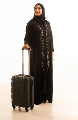 بورتريه لشابة عربية خليجية سعودية محجبة ترتدي العباءة السوداء تمسك حقيبة السفر تنظر الى شىء ما, الشعور بالسعادة والفرح، السياحة في إجازة الصيف, صورة الجسم بالطول الكامل, خلفية بيضاء