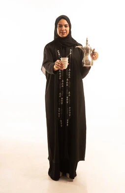 بورتريه لشابة عربية خليجية سعودية ترتدي عباءة سوداء تقوم بصب القهوة من الدلة النحاسية، مفهوم الكرم وحسن الاستقبال، يوم بدينا 1727 م، ذكرى تأسيس الدولة السعودية الاولى 22 فبراير، خلفية بيضاء