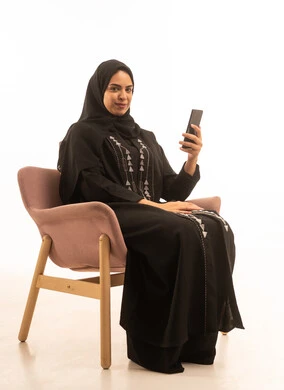 A portrait of a Gulf Arab Saudi woman wearing a black abaya sitting on a comfortable sofa, integrating modern technologies into daily life, communicating with family and friends, with a white background. A portrait of a Gulf Arab Saudi woman wearing a black abaya sitting on a comfortable sofa, integrating modern technologies into daily life, communicating with family and friends, with a white background.