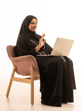 الدردشة و التواصل مع الاهل، بورتريه لسيده عربيه خليجيه سعودية ترتدي العباءه السوداء تحمل بيدها جهاز اللاب توب المحمول، تطور التكنولوجيا والأجهزة التقنية, إستخدام الحاسوب لإنجاز المهام، خلفية بيضاء