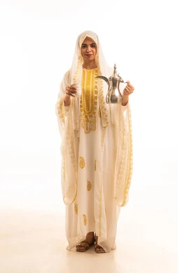 The anniversary of the establishment of the first Saudi state is February 22, the day we began in 1727 AD. A portrait of a young Arab Gulf Saudi woman wearing the shayla and nashl pouring coffee from a brass dallah, embodying the concept of generosity and hospitality, with a white background.