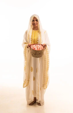 ذكرى تاسيس الدولة السعودية 22فبراير، ارتداء أزياء المنطقة الشرقية، بورتريه مقرب لفتاة عربية خليجية سعودية مبتسمة ترتدي الشيلة والنشل تحمل بيدها سلة قش ممتلئة بالورد الجوري الطبيعي، حرف ومهن يدوية شعبية قديمة، صورة لكامل الجسم، خلفية بيضاء