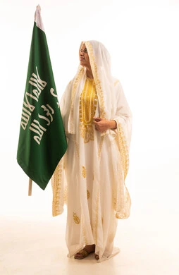 بورتريه لإمرأة عربية خليجية سعودية مبتسمة ترتدي الشيلة والنشل تحمل بيدها علم التأسيس، ذكرى تأسيس الدولة السعودية الأولى، يوم العلم السعودي11 مارس، يوم بدينا 1727 م، ارتداء أزياء المنطقة الشرقية، الاحتفال بالمناسبات والأعياد الوطنية الشعبية، خلفية بيضاء