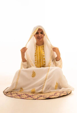 Looking confidently at the camera, wearing the Eastern Province attire for national occasions and holidays, on the day we began in 1727 AD, a portrait of a smiling Arab Gulf Saudi woman wearing the shayla and nashl sitting on a mat in commemoration of the founding of the first Saudi state on February 22, with a white background.