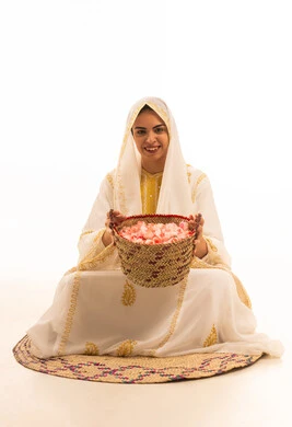 يوم بدينا 1727 م، ذكرى تأسيس الدولة السعودية الاولى 22 فبراير،منتج ومحصول محلى، بورتريه لشابة عربية خليجية سعودية ترتدي العباءة البيضاء تجلس على حصيرة من القش امام سلة مليئة بالورود الى الكاميرا بإيماءات السرور، خلفية بيضاء