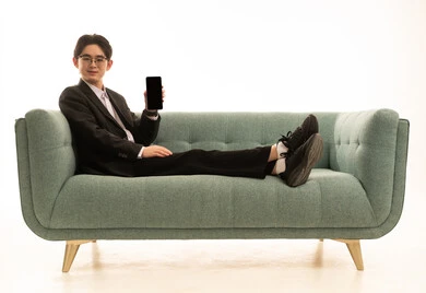 A black screen displayed on the mobile, a portrait of a young Asian man wearing a formal suit sitting on the couch holding a mobile phone, remote work and browsing the internet, using a modern and advanced technical device to complete the project, white background.