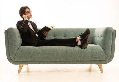 محاولة تذكر شىء ما، بورتريه لشاب اسيوى يرتدى البدلة الرسمية يجلس على الاريكة  يمسك بيده كتاب تثقيفي، الاستمتاع بقراءة الروايات والقصص، خلفية بيضاء