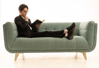 ثقافة التعلم الذاتي ، تعابير التركيز والاندماج، بورتريه لشاب اسيوى يرتدى البدلة الرسمية يجلس على الاريكة  يمسك بيده كتاب تثقيفي، الاستمتاع بقراءة الروايات والقصص، خلفية بيضاء