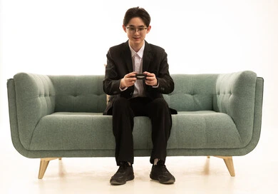 استخدام التكنولوجيا الحديثة في الترفيه بورتريه لشاب اسيوى يرتدى البدلة الرسمية يجلس على كرسى مريح بعصا التحكم، قضاء وقت ممتع في المنزل، المتعة والتسلية والتفاعل ، خلفية بيضاء