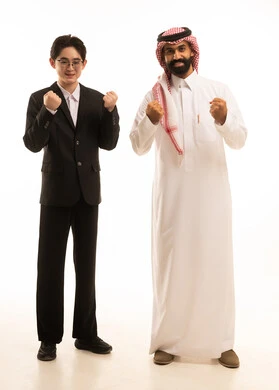 الاندماج بتشجيع فريق كرة القدم، بورتريه لرجل عربي خليجي سعودى يرتدي الثوب التقليدى والشماغ يقف بجانب شاب اسيوى يرتدي البدلة الرسمية يقومان برفع يديهما بتعابير الفوز و الانتصار، الجسم بالطول الكامل، خلفية بيضاء