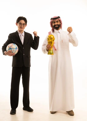 Facial and hand gestures indicating happiness and enthusiasm, a portrait of a Saudi Gulf Arab man wearing traditional attire and a ghutrah holding a trophy standing next to a young man holding the team's ball, both raising their hands with expressions of victory, full-body shot, white background.