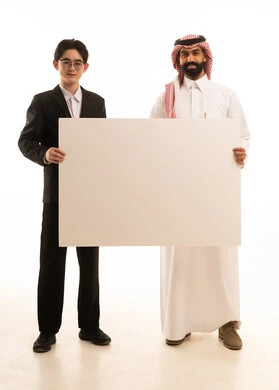 استخدام لوحة توضيحية بيضاء، بورتريه لرجل عربي خليجي سعودى يرتدي الثوب التقليدى والشماغ يقف بجانب شاب اسيوى يرتدي البدلة الرسمية و يحملان موك اب مستطيل كبير، صورة الجسم بالطول الكامل، خلفية بيضاء