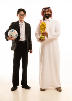 Victory and triumph in the championship, a portrait of a young Asian man wearing a formal suit holding a football in his hands looking at the camera, an Arab Gulf Saudi man wearing traditional attire and a ghutrah holding the championship trophy, full-body image, white background.