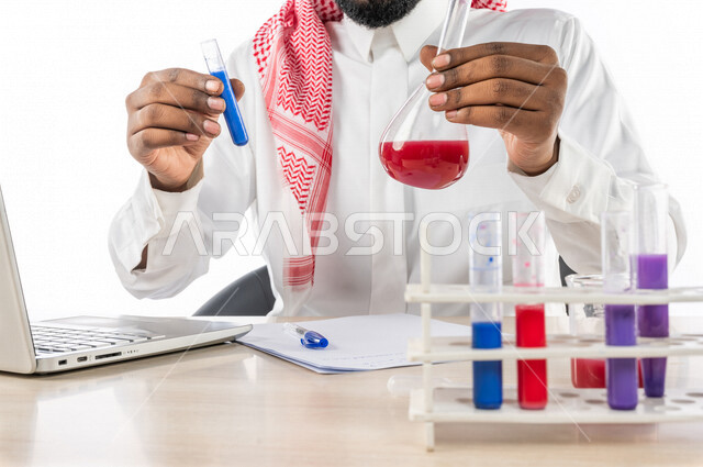 بورتريه لرجل خليجي سعودي ، بالزي السعودي التقليدي ، إستخدام جهاز الحاسوب المحمول، إستخدام انابيب الاختبار لإجراء التجارب، إجراء تجارب وتفاعلات كيميائية في المختبر، تجارب وأبحاث علمية، دراسات وتحاليل، خلفية بيضاء، مختبر ومعمل الكيمياء، البحث والتطوير