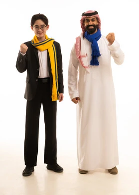 النظر إلى الكاميرا بتفاعل واندماج وحماس, الشغف بمتابعة المباريات الرياضية,  بورتريه لرجل عربي خليجي سعودى يرتدي الثوب التقليدى و الشماغ و وشاح فريق الهلال يقف بجانب شاب اسيوى يرتدي البدلة الرسمية و وشاح فريق النصر يرفعان يديهما بتعابيلر الفوز، خلفية بيضاء