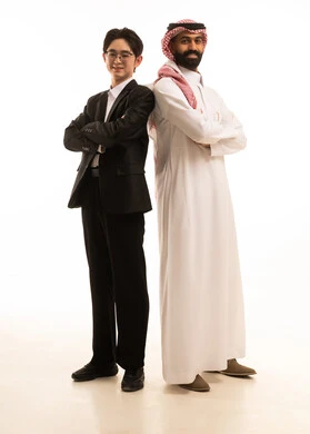 الوقوف بأيدى متقاطعة، بورتريه لرجل عربي خليجي سعودى يرتدي الثوب التقليدى والشماغ يقف و ظهره الى ظهر شاب اسيوى يرتدي البدلة الرسمية ينظران الى الكاميرا بثقة، الجسم بالطول الكامل، خلفية بيضاء
