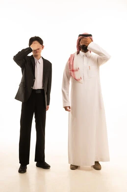 The feeling of shame and embarrassment, closing the eyes and not wanting to see, experiencing shock and disbelief, a portrait of a Saudi Gulf Arab man wearing traditional attire and a ghutrah standing next to an Asian young man in a formal suit, covering their faces with their hands, full-body image, white background.