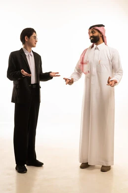 Hesitation and lack of confidence regarding a certain matter, a portrait of a Saudi Gulf Arab man wearing traditional attire and a shemagh standing next to a Chinese young man in a formal suit, both raising their hands in gestures of uncertainty, feeling confused and uninformed, with a white background.
