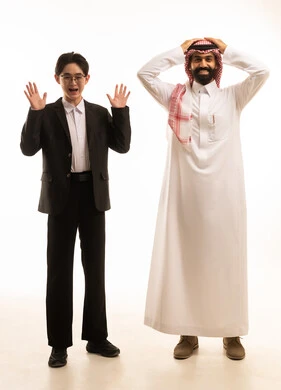 بورتريه لرجل عربي خليجي سعودى يرتدي الثوب التقليدى والشماغ يتحاور مع شاب اسيوى يرتدي البدلة الرسمية يرفعان أيديهم للأعلى بتعابيرالتفاجؤ لرؤية شيء ما, حركة وجه وفم تدل على الصدمة و الدهشة، صورة الجسم بالطول الكامل، خلفية بيضاء .