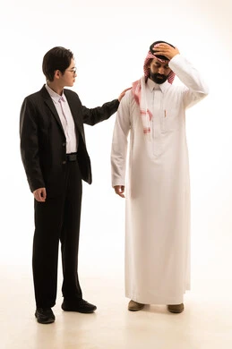 مفهوم التعاطف والمودة بين الزملاء، بورتريه لشاب صينى يرتدي البدلة الرسمية  يضع يده على كتف رجل عربي خليجي سعودى يرتدى الثوب التقليدى والشماغ لتخفيف الالم والمواساة، صورة الجسم بالطول الكامل، خلفية بيضاء