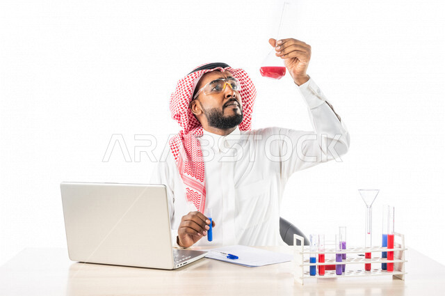 بورتريه لرجل خليجي سعودي ، بالزي السعودي التقليدي ، إستخدام جهاز الحاسوب المحمول، إستخدام انابيب الاختبار لإجراء التجارب، إجراء تجارب وتفاعلات كيميائية في المختبر، تجارب وأبحاث علمية، دراسات وتحاليل، خلفية بيضاء، مختبر ومعمل الكيمياء، البحث والتطوير