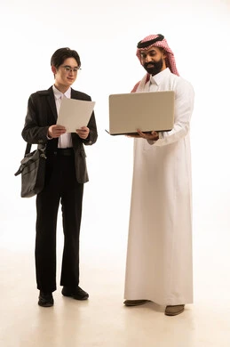 استخدام التقنية الحديثة في انجاز العمل, استضافة رجال الاعمال الاجانب في المملكة, عقد اتفاقية عمل جديدة، بورتريه لرجل عربي خليجي سعودي يرتدي الزي التقليدي يحمل اللابتوب يقف بجانب شاب صيني يرتدي البدلة الرسمية و حقيبة سوداء يحمل تقارير العمل، خلفية بيضاء