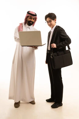 استخدام التقنية الحديثة، بورتريه لشاب اسيوى يرتدي البدلة الرسمية  يقف بجانب رجل عربي خليجي سعودى يرتدي الثوب التقليدى والشماغ يقومان بالعمل على الحاسوب المحمول، تبادل الخبرة والمعرفة بين البلاد, خلفية بيضاء