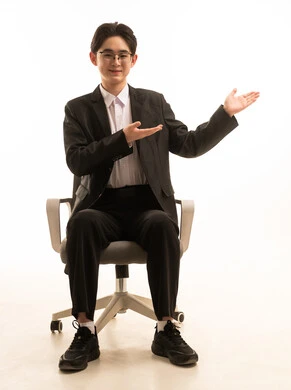 ايماءاة تحديد موقع معين، حركة تدل على هذا المكان (هنا)، بورتريه لرجل اسيوى يرتدى البدلة الرسمية يجلس على كرسي مريح يشيربيديه الى شيء ما، خلفية بيضاء