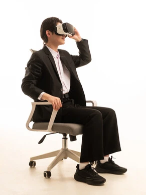 ، المتعة و التسلية بالمشاهدة عبر نظارة الواقع الافتراضي، بورتريه لشاب اسيوى يرتدى البدلة الرسمية يجلس على الكرسي ينظر من خلال نظارات ثلاثية الأبعاد, الاندماج ومحاكاة العالم الخيالي، التطورالتقني والتكنولوجي, خلفية بيضاء