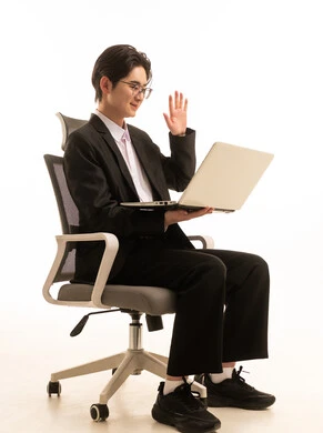 اجراء مكالمة فيديو عبر الحاسوب، بورتريه لرجل اسيوى يرتدي البدلة الرسمية يجلس على كرسى يحمل اللابتوب و يقوم بالقاء التحية, العمل عن بعد, التسوق الإلكتروني السريع والآمن، استخدام جهاز تقني حديث متطور، خلفية بيضاء