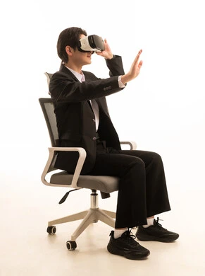 Technological and technical development, enjoyment and entertainment through watching via virtual reality glasses, a portrait of an Asian young man wearing a formal suit sitting on a chair looking through 3D glasses, immersion and simulation of the imaginary world, white background.