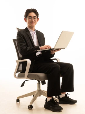 بورتريه لرجل اسيوى يرتدي البدلة الرسمية يجلس على كرسى يحمل الحاسوب ينظر الى الكاميرا بتعابير السرور, العمل عن بعد, التسوق الإلكتروني السريع والآمن، استخدام جهاز تقني حديث متطور، خلفية بيضاء