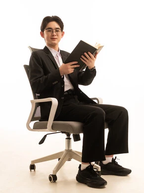Looking at the camera with expressions of joy, practicing the hobby of reading, the concept of passion for reading, the culture of self-learning, a portrait of an Asian man wearing a formal suit sitting on a chair holding a book, white background.
