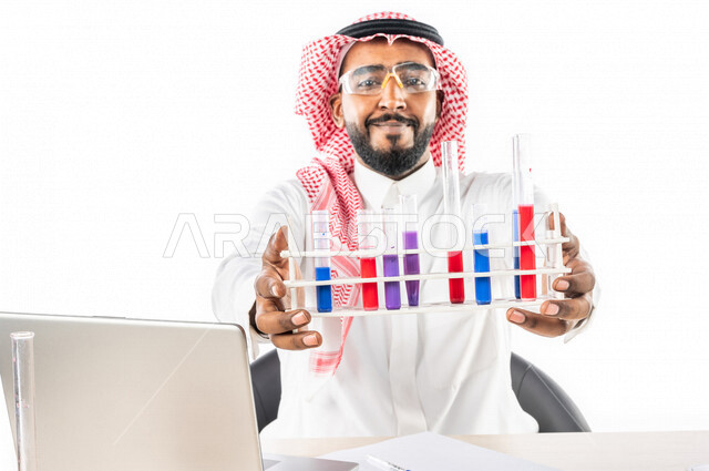 بورتريه لرجل خليجي سعودي ، بالزي السعودي التقليدي ، إستخدام جهاز الحاسوب المحمول، إستخدام انابيب الاختبار لإجراء التجارب، إجراء تجارب وتفاعلات كيميائية في المختبر، تجارب وأبحاث علمية، دراسات وتحاليل، خلفية بيضاء، مختبر ومعمل الكيمياء، البحث والتطوير