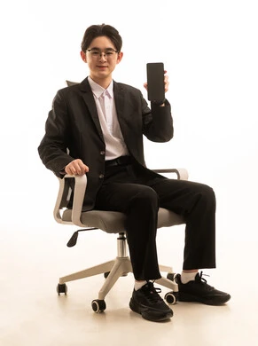 عرض شاشة سوداء عبر الجوال، بورتريه لرجل اسيوى يرتدى البدلة الرسمية يجلس على كرسي مريح يمسك الهاتف المحمول بتعابير السعادة, استخدام جهاز تقنى حديث، إرسال الرسائل النصية والصوتية عبر الجوال، خلفية بيضاء