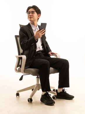 التواصل مع الاهل والاصدقاء، بورتريه لرجل اسيوى يرتدى البدلة الرسمية يجلس على كرسي مريح يمسك الهاتف المحمول بتعابير السعادة, استخدام جهاز تقنى حديث، خلفية بيضاء