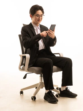 إرسال رسالة نصية و صوتية عبر الجوال، بورتريه لرجل اسيوى يرتدى البدلة الرسمية يجلس على كرسي مريح يمسك الهاتف المحمول بتعابير السعادة, استخدام جهاز تقنى حديث، خلفية بيضاء
