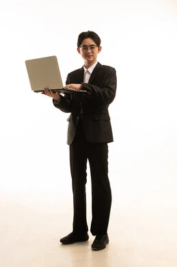 بورتريه لرجل اسيوى يرتدي البدلة الرسمية يحمل اللاب توب ينطر الى الكاميرا, التسوق الإلكتروني السريع والآمن، العمل عن بعد، إستخدام جهاز تقنى حديث، صورة للجسم بالطول الكامل, خلفية بيضاء