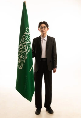 ذكرى اليوم الوطني السعودي 23 سبتمبر، بورتريه لرجل اسيوى يرتدي البدلة الرسمية يحمل بيده علم المملكة ينظر الى الكاميرا، الجسم بالطول الكامل، يوم العلم 11 مارس, خلفية بيضاء