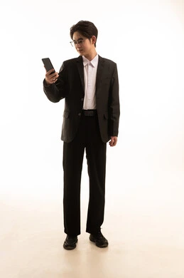 التواصل مع العائلة عبر الجوال, استخدام الأجهزة التقنية المتطورة, بورتريه لرجل اسيوى يرتدي البدلة الرسمية يمسك الهاتف المحمول بيده وينظر اليه, صورة للجسم بالطول الكامل, خلفية بيضاء
