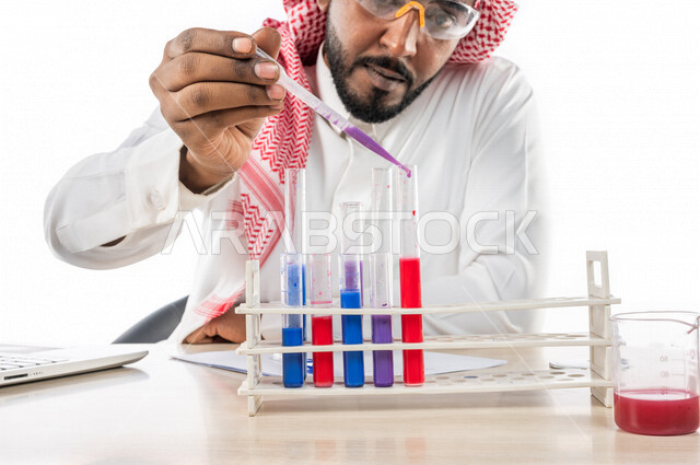 بورتريه لرجل خليجي سعودي ، بالزي السعودي التقليدي ، إستخدام جهاز الحاسوب المحمول، إستخدام انابيب الاختبار لإجراء التجارب، إجراء تجارب وتفاعلات كيميائية في المختبر، تجارب وأبحاث علمية، دراسات وتحاليل، خلفية بيضاء، مختبر ومعمل الكيمياء، البحث والتطوير