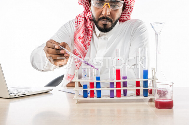 بورتريه لرجل خليجي سعودي ، بالزي السعودي التقليدي ، إستخدام جهاز الحاسوب المحمول، إستخدام انابيب الاختبار لإجراء التجارب، إجراء تجارب وتفاعلات كيميائية في المختبر، تجارب وأبحاث علمية، دراسات وتحاليل، خلفية بيضاء، مختبر ومعمل الكيمياء، البحث والتطوير