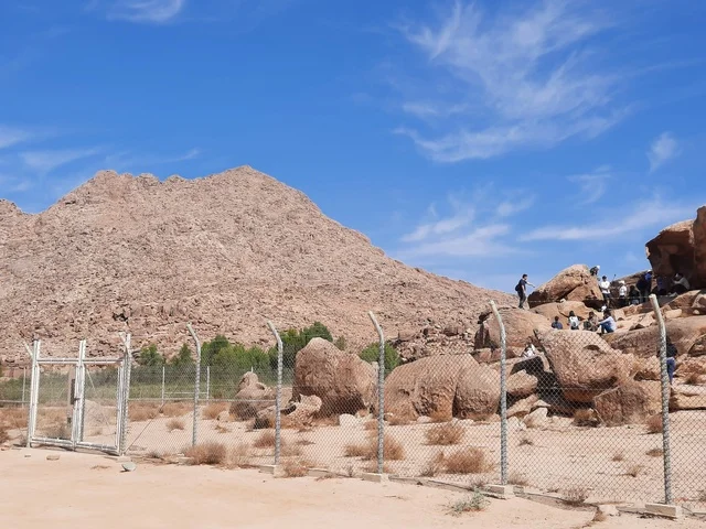 The archaeological site is surrounded by barbed wire, dry grass in desert areas, safari trips and enjoyable recreational activities in Al-Ula, tourist attractions in the desert regions of the Kingdom, rock formations and structures in the middle of the Saudi desert, ancient historical archaeological landmarks.