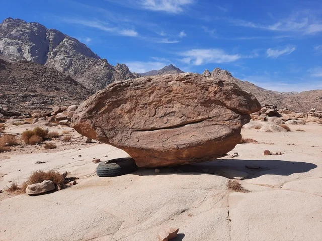 A large rock in the middle of the desert, dry grasses in desert areas, safari trips and fun recreational activities in Al-Ula, tourist attractions in the desert regions of the Kingdom, rock formations and structures in the middle of the Saudi desert, ancient historical archaeological sites.