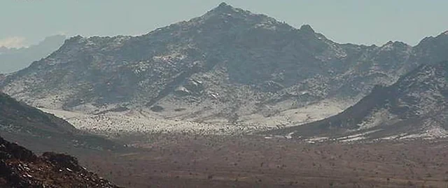 The foggy atmosphere above the peaks and mountain heights, a famous tourist place and area, the natural mountainous terrain in the Kingdom of Saudi Arabia, the growth of wild and thorny plants, the rock formations and structures.