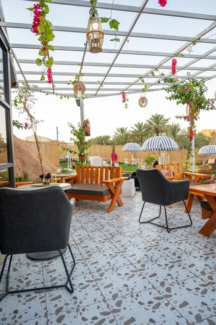 منطقة جلوس خارجية في مقهى بقرية عقدة، طابع ريفي وسط الجبال وأشجار النخيل، نسيم الجبال البارد، تجربة تجمع بين الراحة والهدوء والطبيعة في أحد مواقع ومعالم السياحة فى مدينة حائل بالمملكة العربية السعودية