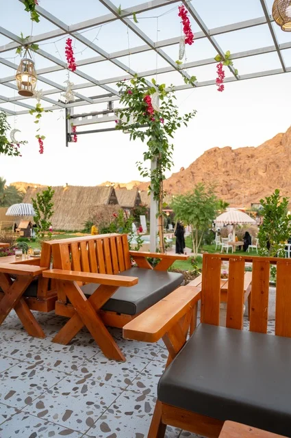 منطقة جلوس خارجية في مقهى بقرية عقدة، طابع ريفي وسط الجبال وأشجار النخيل، نسيم الجبال البارد، تجربة تجمع بين الراحة والهدوء والطبيعة في أحد مواقع ومعالم السياحة فى مدينة حائل بالمملكة العربية السعودية