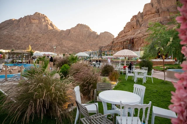An outdoor seating area in a café in the village of Aqda, with a rustic character amidst the mountains and palm trees, a cool mountain breeze, an experience that combines comfort, tranquility, and nature in one of the tourist sites and landmarks in the city of Hail, Saudi Arabia.